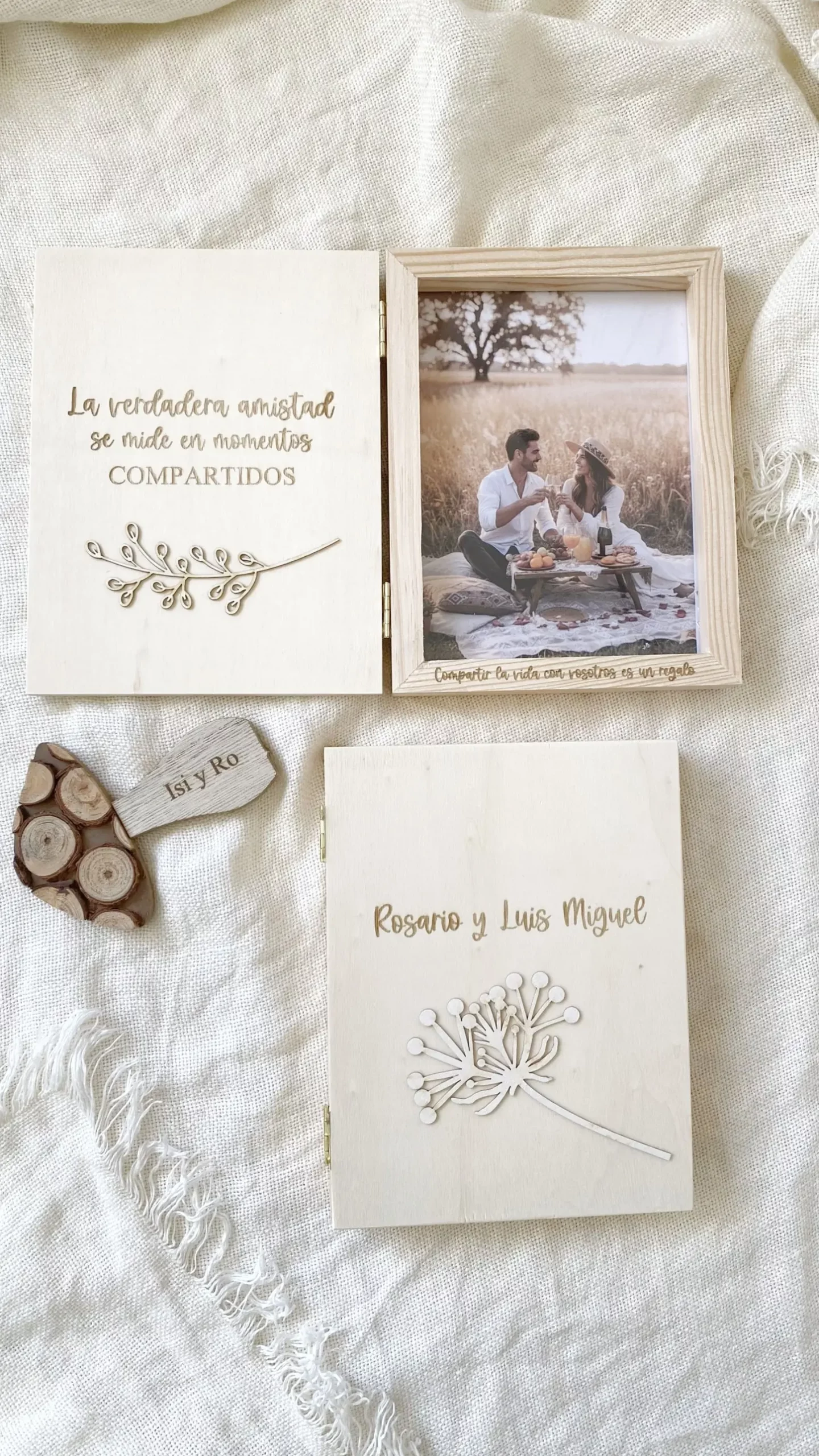 Álbum de madera abierto con frase de amistad grabada y foto de pareja, junto a otro álbum cerrado con nombres