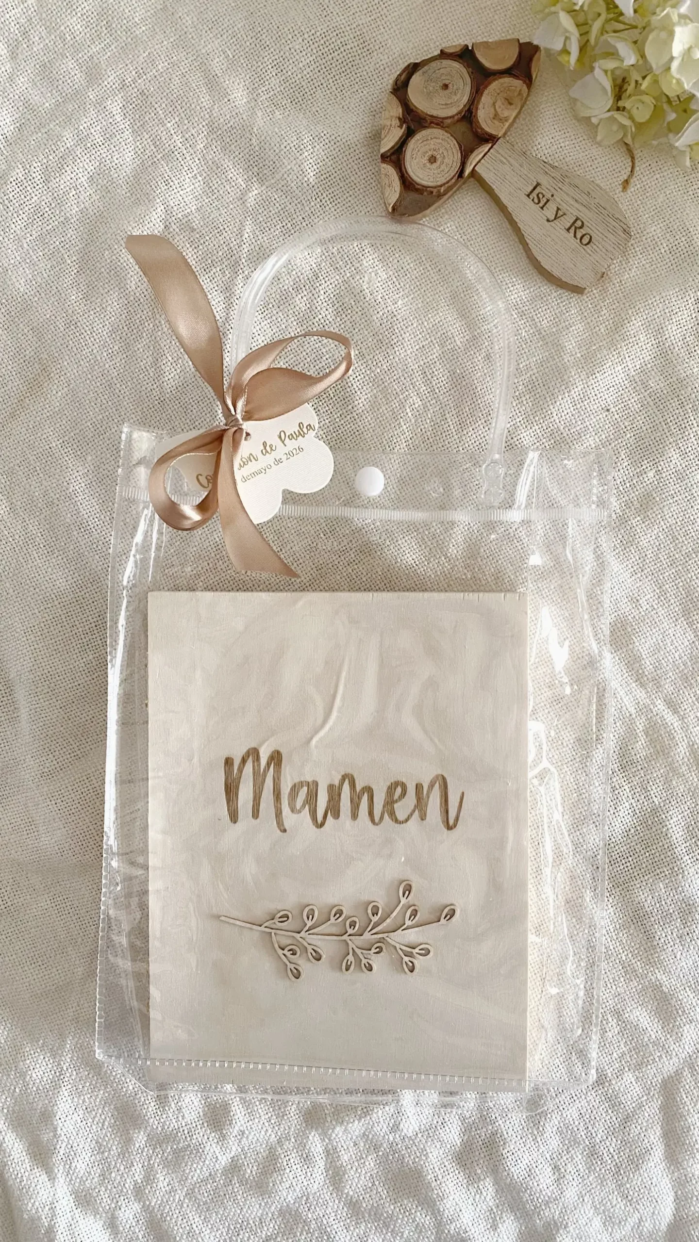 Álbum de madera con nombre y ramita decorativa dentro de bolsa de regalo transparente con lazo de raso