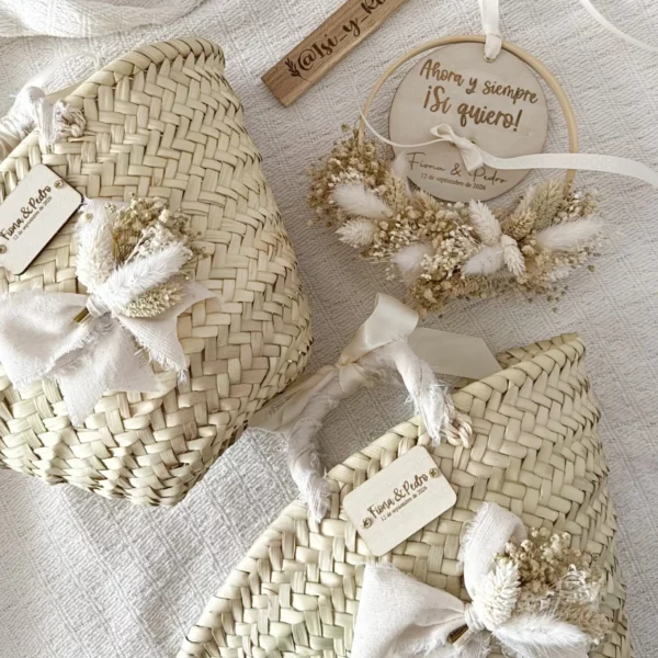 Dos cestos de palma personalizados para damitas de boda con lazo de lino y flores secas junto a un aro portaalianzas
