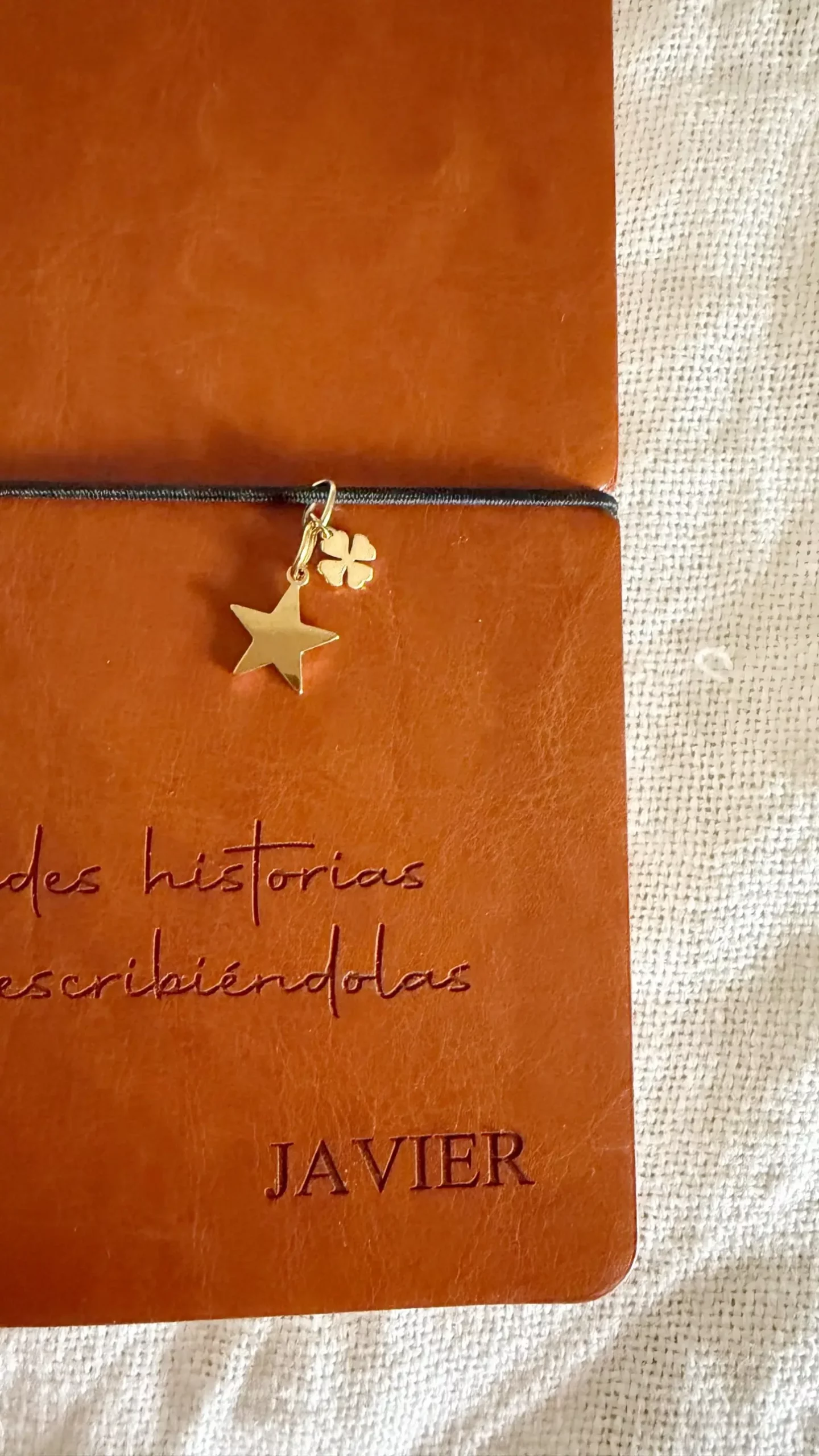 Detalle del charm dorado de estrella y trébol y el nombre grabado en la cubierta del cuaderno personalizado