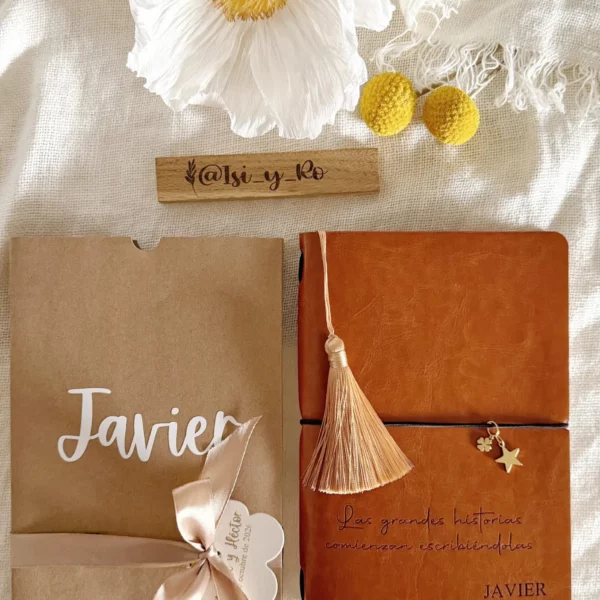 Cuaderno de cubierta efecto piel con borla junto a su funda kraft personalizada con nombre y lazo
