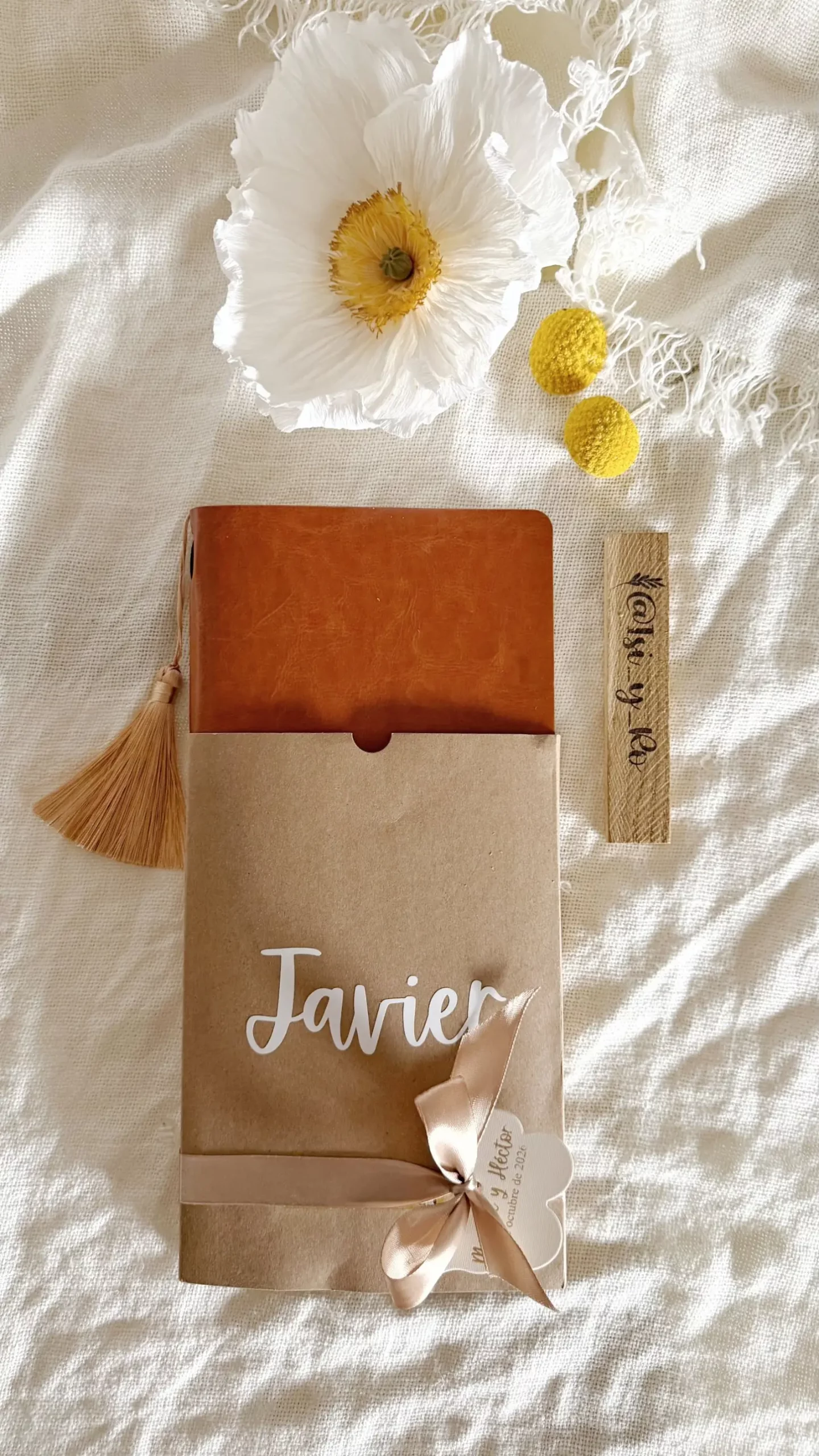 Cuaderno personalizado saliendo de su funda kraft con nombre en vinilo blanco y lazo de raso