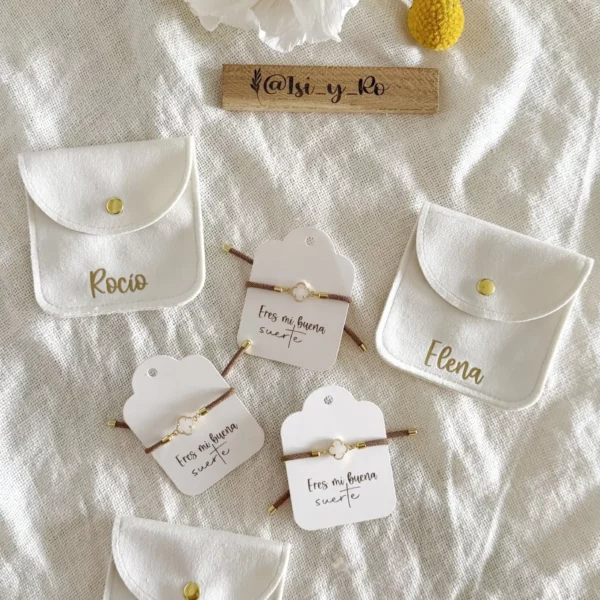 Detalle de pulseras de cordón marrón con trébol de nácar y dorado sobre tarjeta "Eres mi buena suerte"