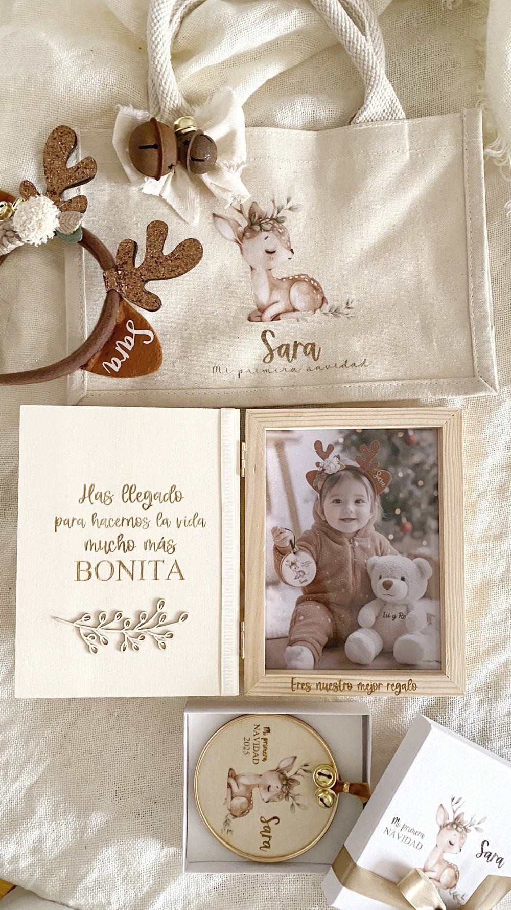 Álbum de fotos de madera abierto con marco y foto de bebé con diadema de reno, y el mensaje “Eres nuestro mejor regalo”